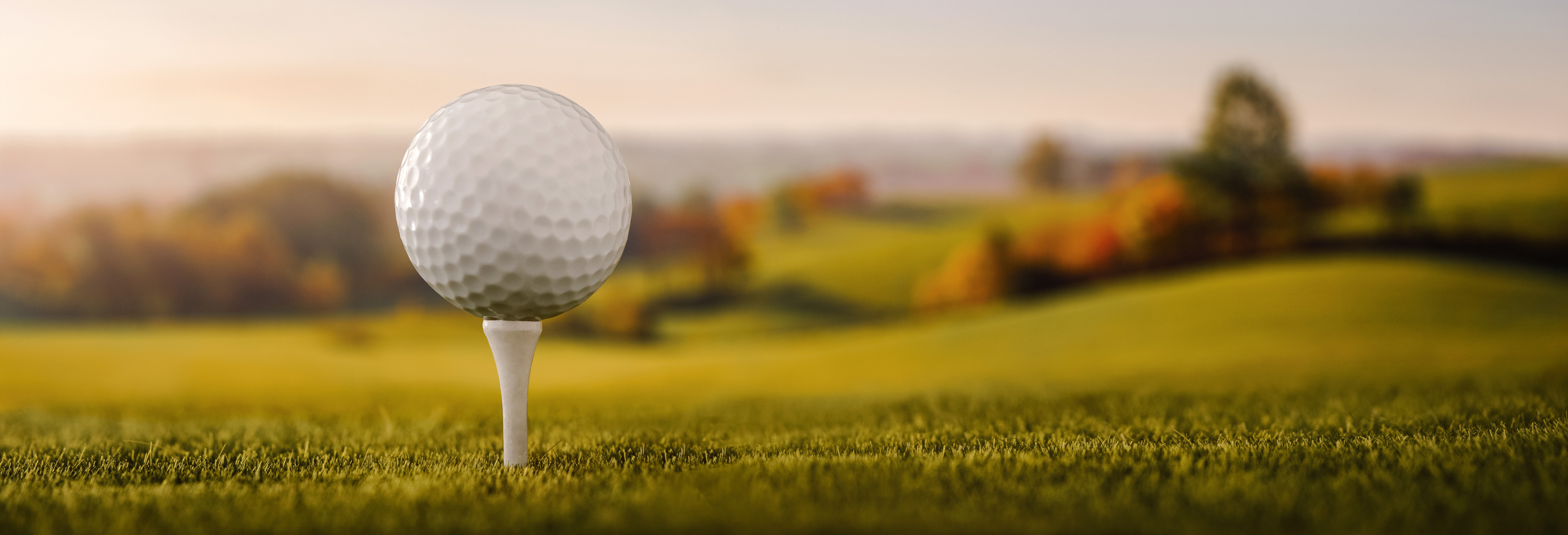 Balle de golf sur un tee devant un parcours au soleil couchant