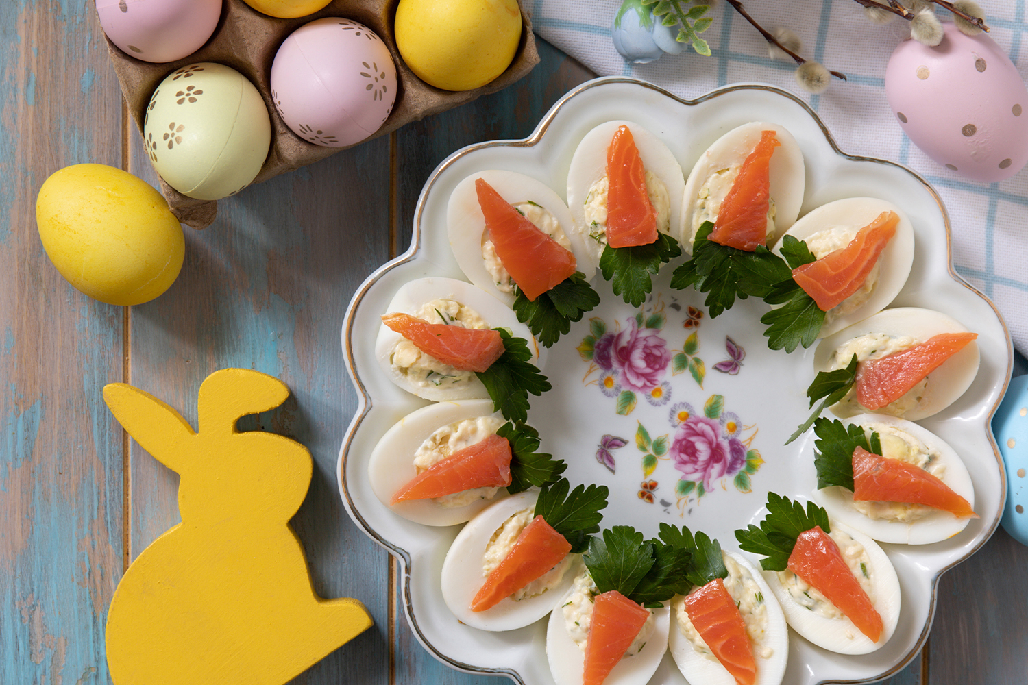 Gefüllte Eier (Deviled Eggs) mit Lachs und Petersilie, angerichtet auf einer Platte, umgeben von bunten Ostereiern und Frühlingsdeko